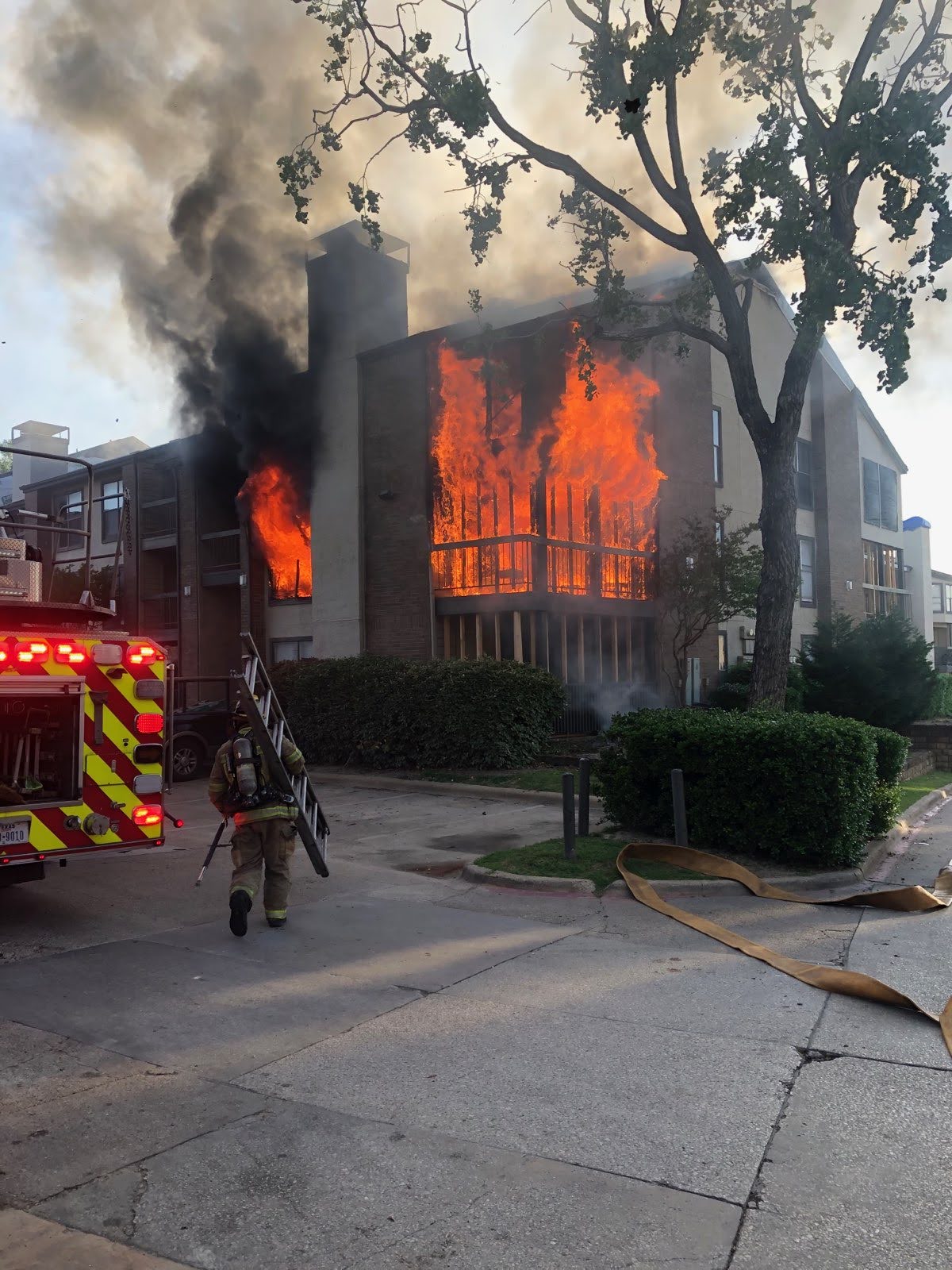 Dallas firefighter carrying a ladder to a burning apartment building