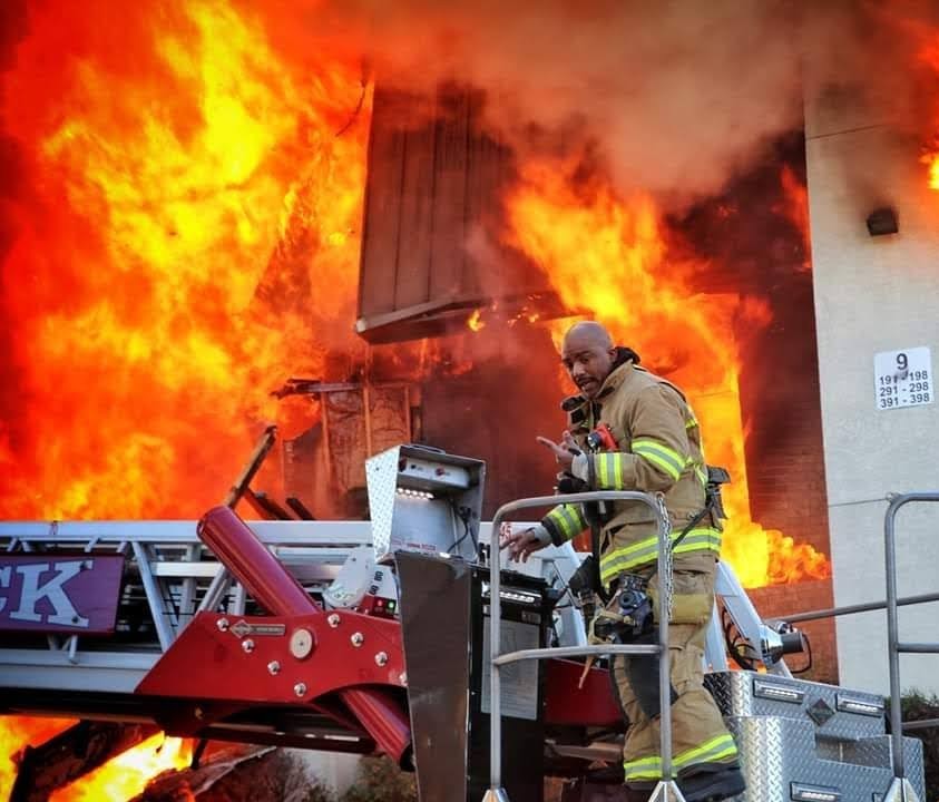 Dallas firefighter on an aerial ladder against a wall of flames
